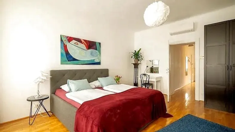 Helles Schlafzimmer mit Doppelbett, Holzboden, Klimaanlage und moderner Kunst an der Wand.