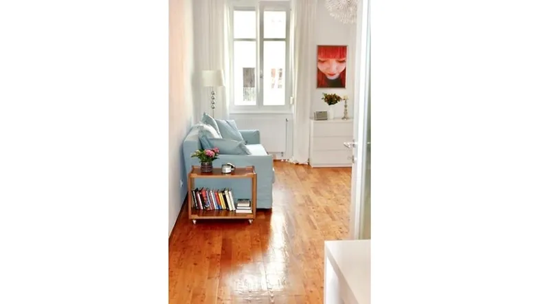 Helles Wohnzimmer mit Holzboden, einem hellblauen Sofa und einem Fenster mit Blick nach draußen.