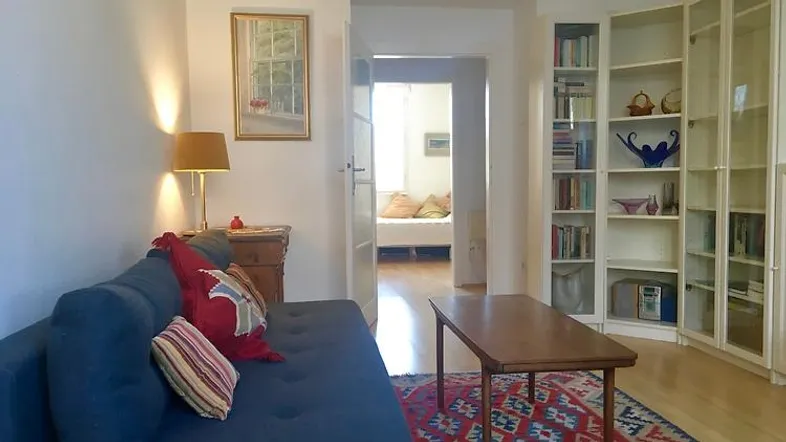 Gemütliches Wohnzimmer mit Sofa, Couchtisch und Bücherregal, das zu einem weiteren Raum führt.