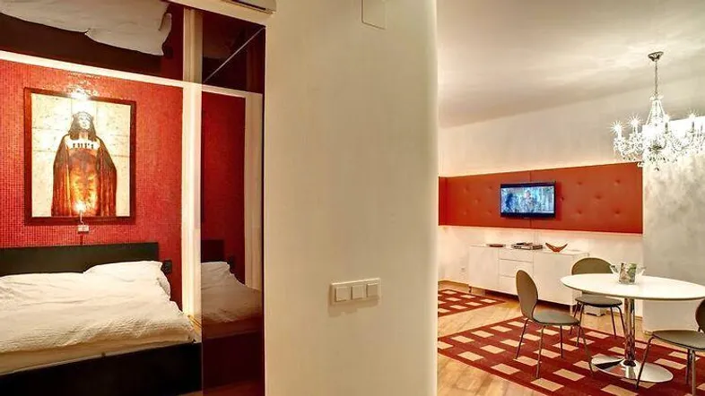 Schlafzimmer mit roter Akzentwand, Kunstwerk und offenem Übergang zum Wohnbereich.
