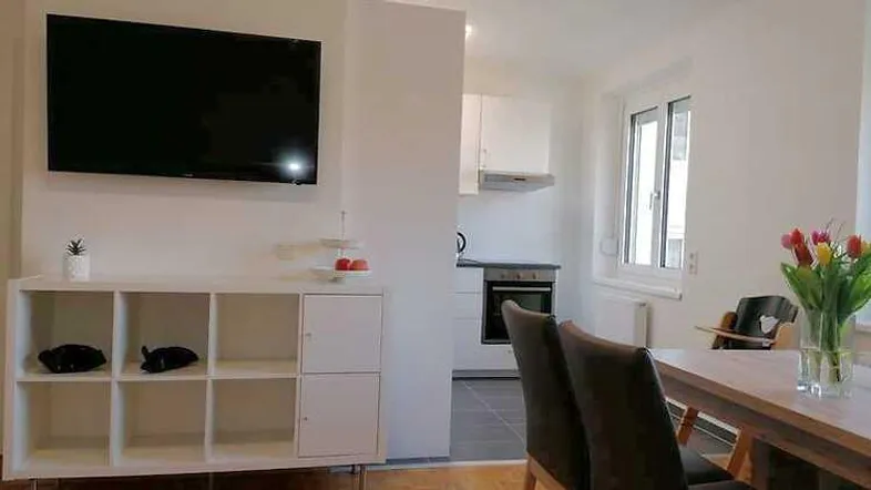Heller Wohn- und Essbereich mit Fernseher, Regal und Blick auf die angrenzende Küche.