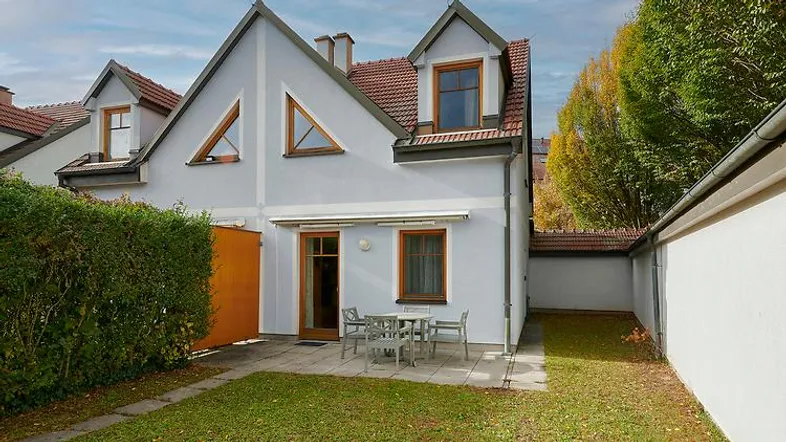 Rückseite des Hauses mit kleiner Terrasse, Gartenbereich und Sitzgelegenheiten im Freien.