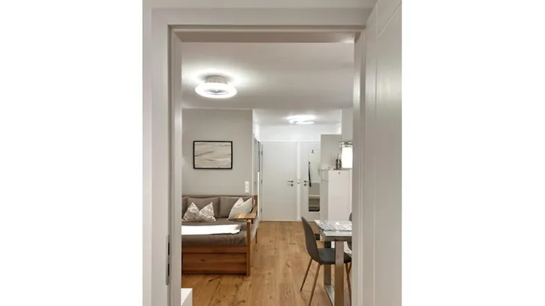 Helles Wohn- und Esszimmer mit Holzboden und moderner Einrichtung, gesehen durch einen Türrahmen.