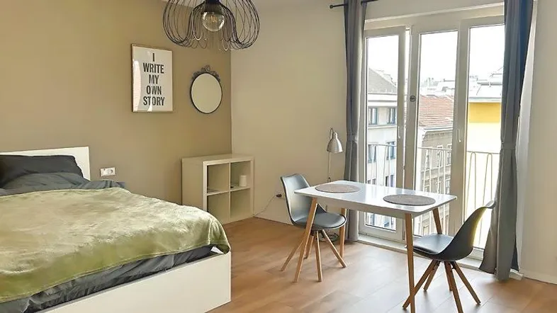 Helles Schlafzimmer mit modernem Bett, Esstisch und Zugang zu einem kleinen Balkon.