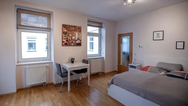 Helles Schlafzimmer mit Holzboden, einem Bett und einem kleinen Essbereich am Fenster.