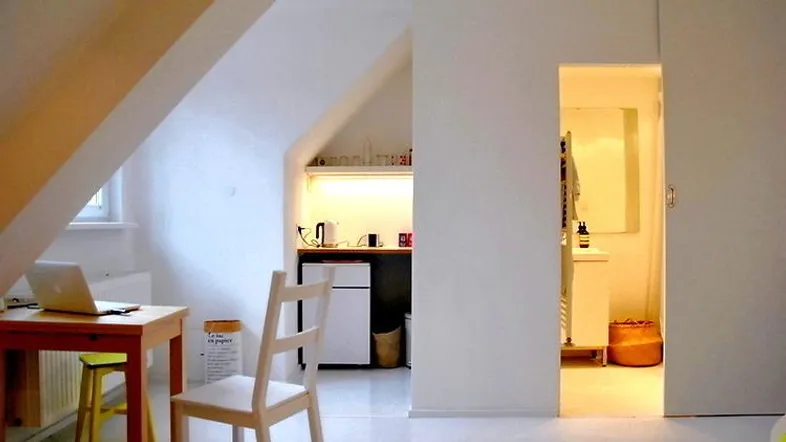 Heller Dachbodenraum mit Schreibtischbereich, kleiner Küchenzeile und Zugang zum Badezimmer.