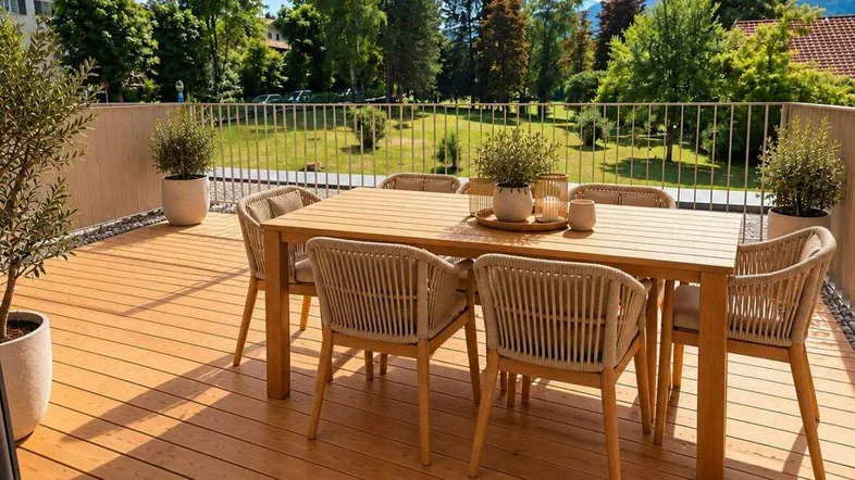 Geräumiger Balkon mit Holzboden, Esstisch und Blick ins Grüne, ideal für Mahlzeiten im Freien.