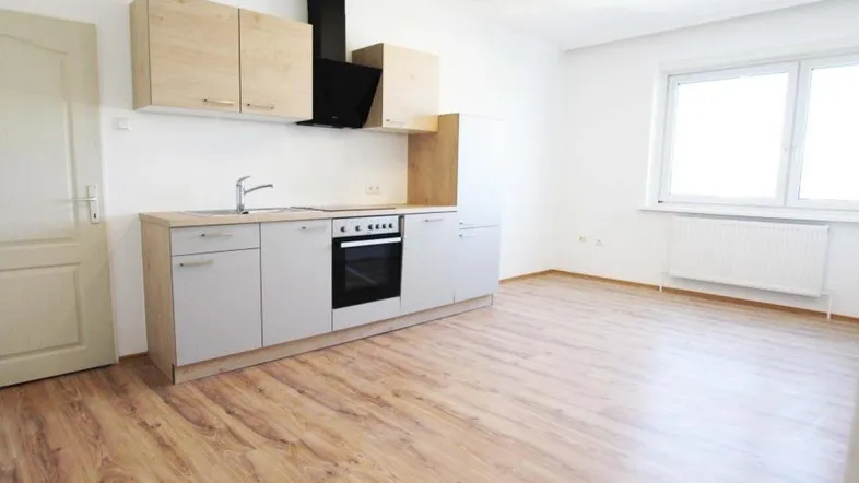 Helle, offene Küche mit Laminatboden, Einbaugeräten und Holz-Optik-Schränken in einem geräumigen Zimmer.