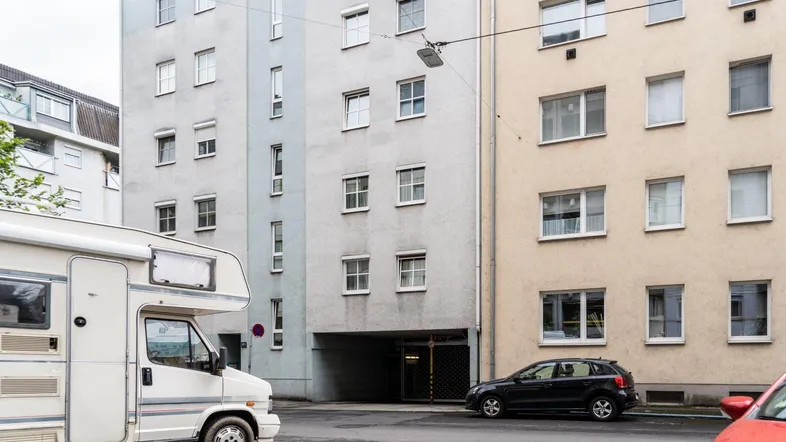 Fassadenansicht von zwei Mehrfamilienhäusern mit Straße und geparkten Fahrzeugen.