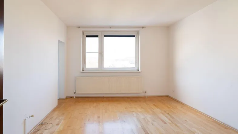 Helles, leeres Zimmer mit Parkettboden und großem Fenster, bereit zur individuellen Gestaltung.