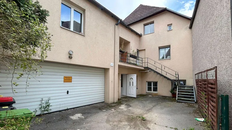 Mehrfamilienhaus mit Garagenzufahrt und Außentreppe zu den oberen Wohnungen.