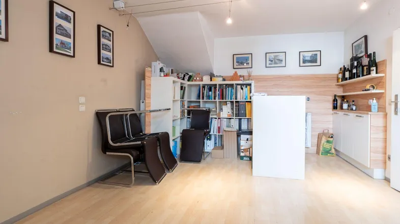 Helles Büro mit Holzboden, Regalen und einer kleinen Küchenzeile, ideal für geschäftliche Nutzung.