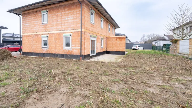 Rückseite der Doppelhaushälfte im Rohbau mit unfertiger Terrasse und unbebautem Gartenbereich.
