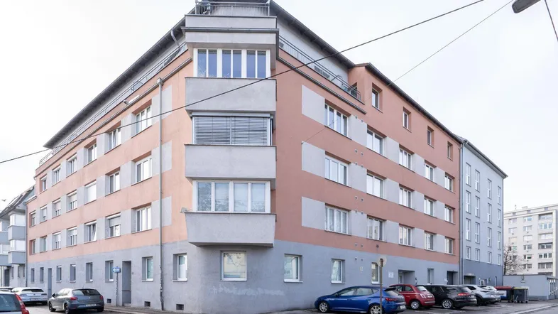 Eckgebäude mit moderner Architektur und vielen Fenstern, umgeben von parkenden Autos.