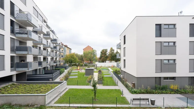 Moderner Innenhof mit Grünflächen, Spielplatz und Wohngebäuden mit Balkonen.