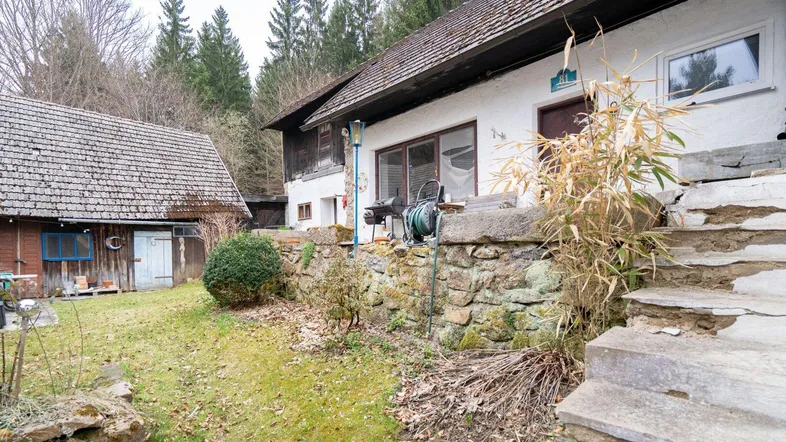 Rustikales Bauernhaus mit Steinterrasse und Gartenbereich, umgeben von Bäumen und Natur.
