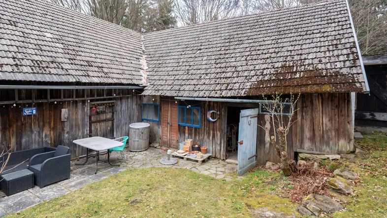 Rustikales Nebengebäude mit kleiner Terrasse und Sitzgelegenheiten im Freien, umgeben von Natur.