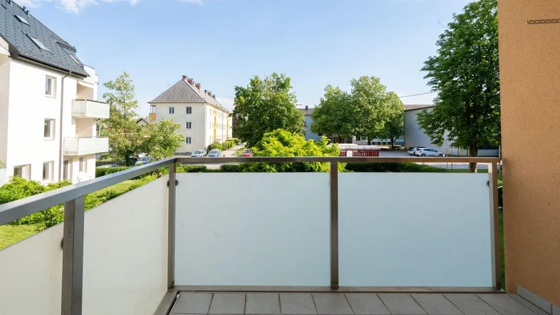Heller Balkon mit Blick auf die umliegenden Wohngebäude und grüne Bäume unter blauem Himmel.
