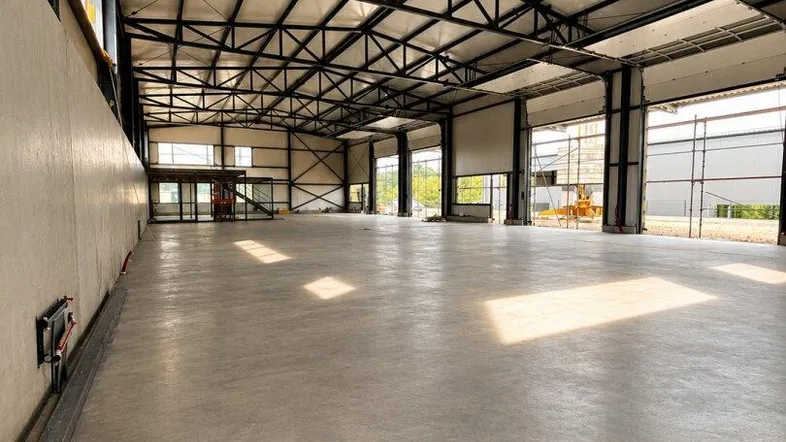 Geräumige Industriehalle mit hohen Decken, sichtbaren Stahlträgern und großen Toren für vielseitige Nutzung.