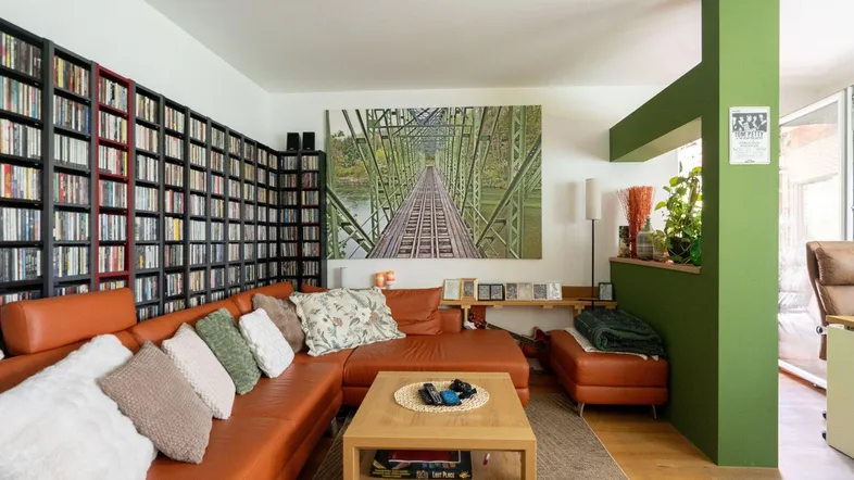 Gemütliches Wohnzimmer mit Ledersofa, Bücherregal und grüner Akzentwand.
