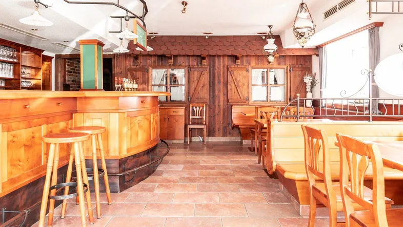 Gemütlicher Restaurantbereich mit Holztheke, traditionellen Möbeln und Terrakotta-Fliesenboden, der eine warme Atmosphäre schafft.