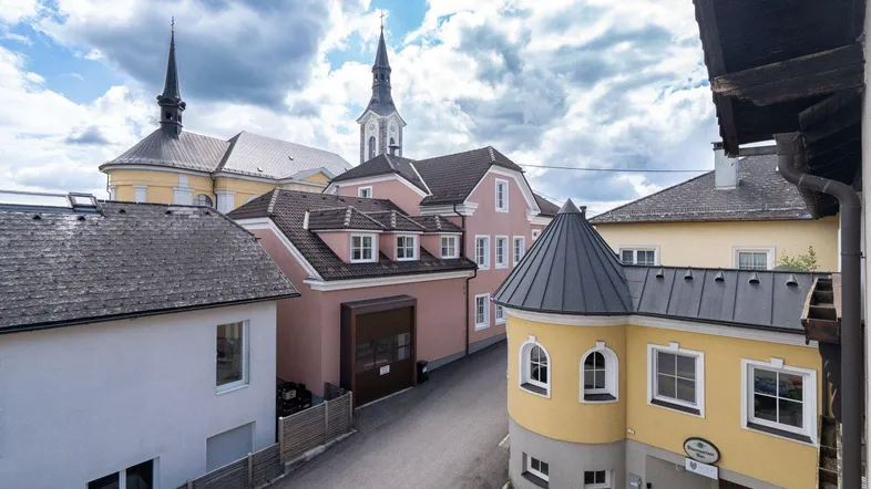 Blick über eine Gasse mit traditionellen Gebäuden und Kirchtürmen unter bewölktem Himmel.