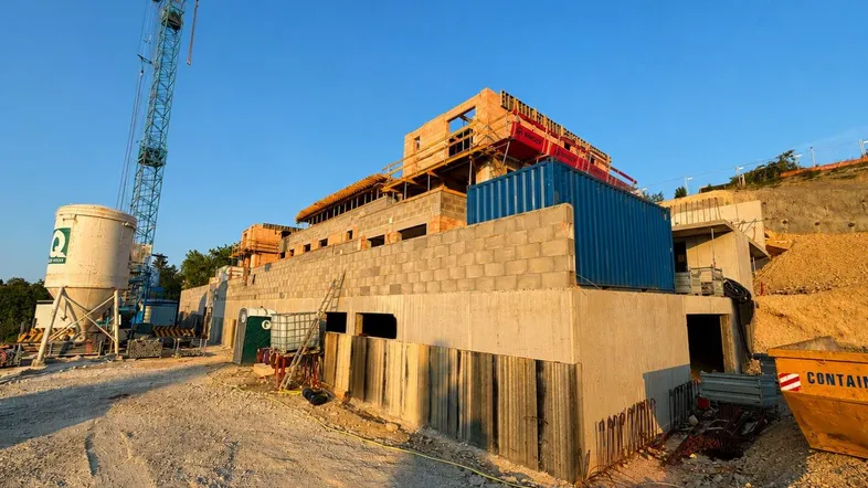 Baustelle eines neuen Gebäudes mit Kran, Baucontainern und Erdarbeiten bei Sonnenuntergang.