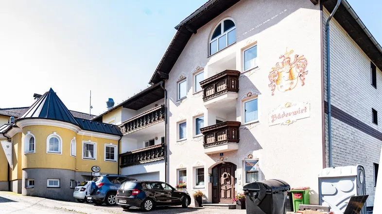 Fassade eines traditionellen Gebäudes mit Balkonen und Parkplätzen davor unter blauem Himmel.