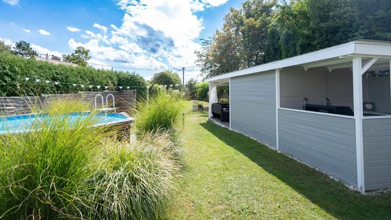 Gartenweg zwischen hohen Gräsern, mit Pool und einem überdachten Bereich für eine Außenküche.