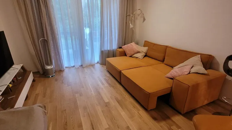 Gemütliches Wohnzimmer mit einem großen orangefarbenen Sofa, hellem Holzboden und Zugang zu einem Balkon.