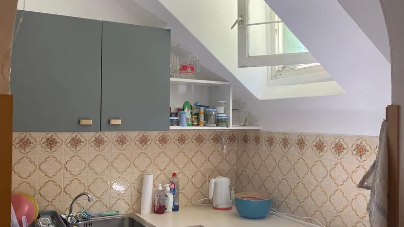 Kleine Küche mit Dachschräge, Einbauschränken, Herd und Spüle, beleuchtet durch ein Dachfenster.
