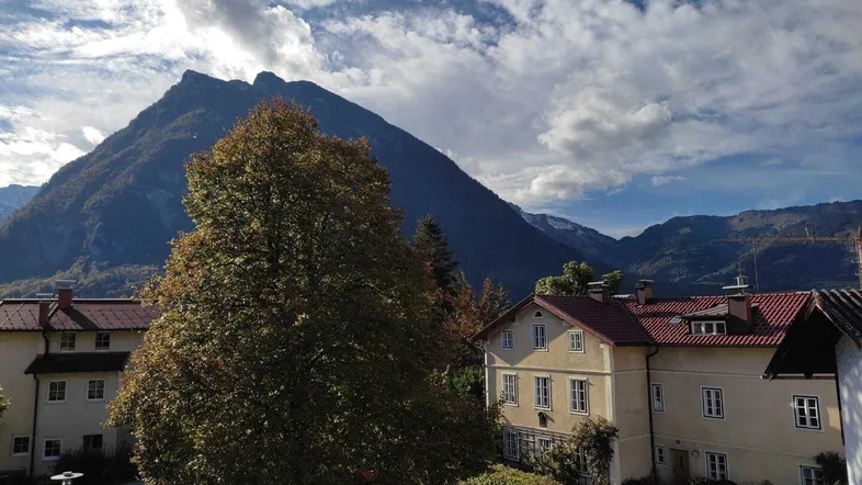 Panoramablick auf majestätische Berge und traditionelle Gebäude unter einem dynamischen Himmel.