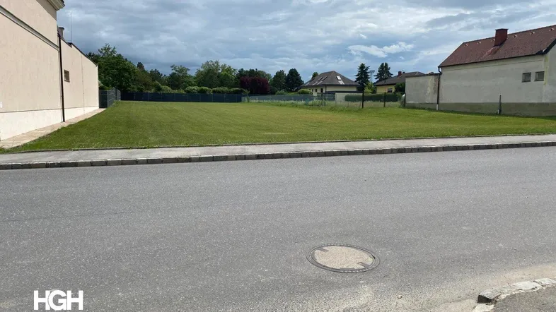 Großes, unbebautes Grundstück mit Rasenfläche und angrenzender Straße unter bewölktem Himmel.
