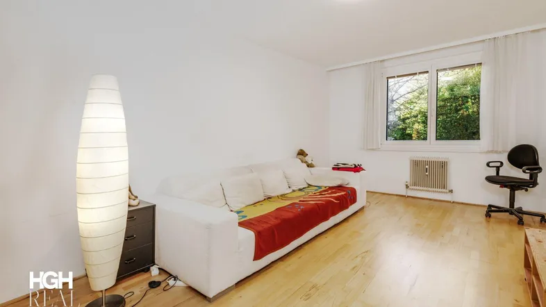 Helles Wohnzimmer mit Parkettboden, weißem Sofa und Blick ins Grüne durch das Fenster.