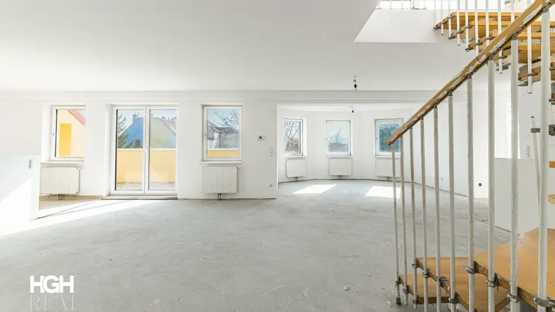 Heller, unmöblierter Raum mit vielen Fenstern, Betonboden und einer Holztreppe, bereit zur Gestaltung.
