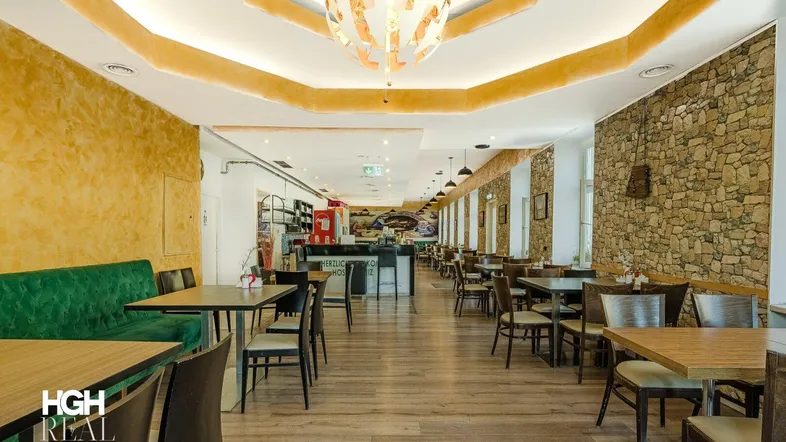 Geräumiger Restaurantbereich mit Holzboden, Steinwand und gemütlichen Sitzgelegenheiten, gut beleuchtet.