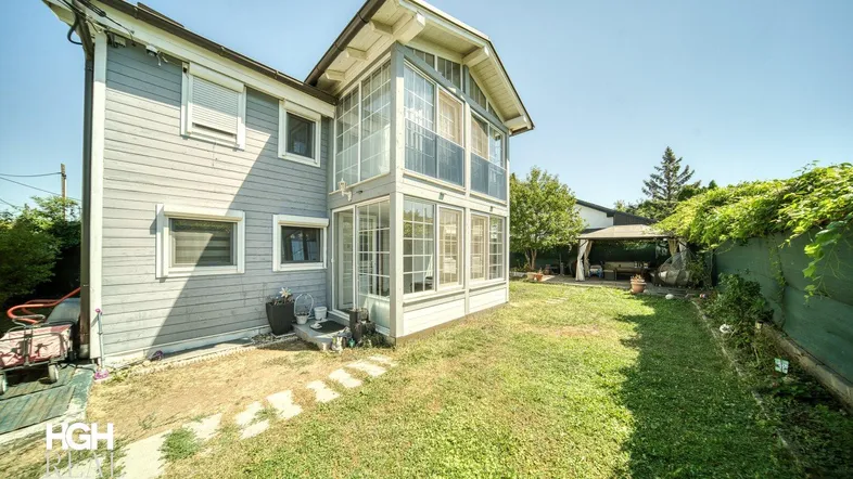 Außenansicht des Hauses mit verglastem Anbau, Rasenfläche und einem Gartenpavillon im Hintergrund.