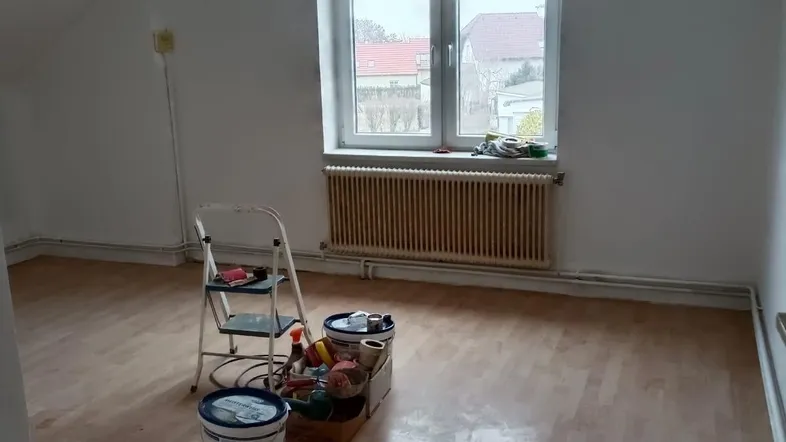 Helles Zimmer im Dachgeschoss mit Laminatboden und Blick nach draußen, bereit für Renovierungsarbeiten.