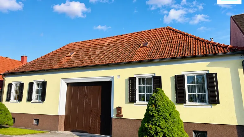 Gelbes Haus mit roten Dachziegeln, schwarzen Fensterläden und gepflegtem Vorgarten.