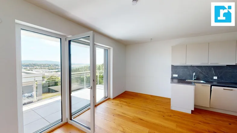 Helles Wohnzimmer mit integrierter Küchenzeile, Holzboden und Zugang zur Terrasse mit Weitblick.