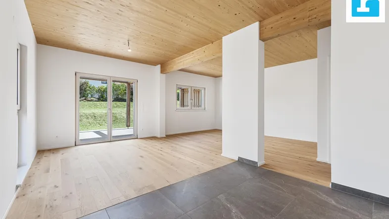 Heller offener Wohnbereich mit Holzbalkendecke, Parkettboden und Zugang zum Garten.