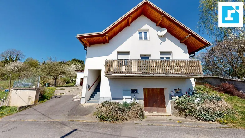 Vorderansicht des traditionellen Hauses mit Holzbalkon und Satteldach unter blauem Himmel.
