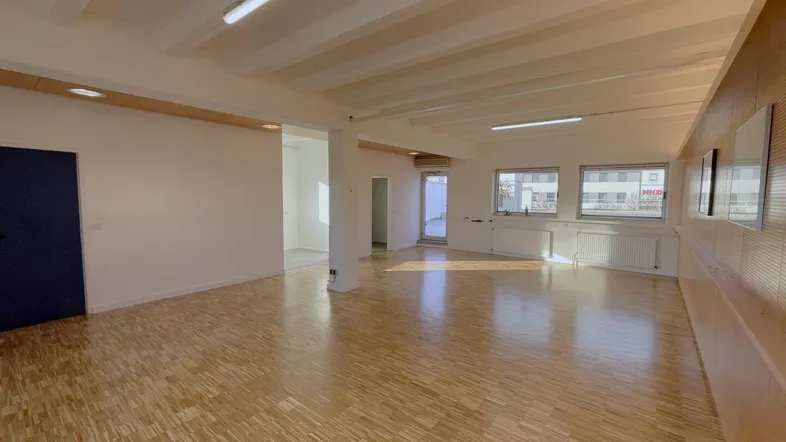 Geräumiger, heller Gewerberaum mit Parkettboden und großen Fenstern, ideal für verschiedene Nutzungen.