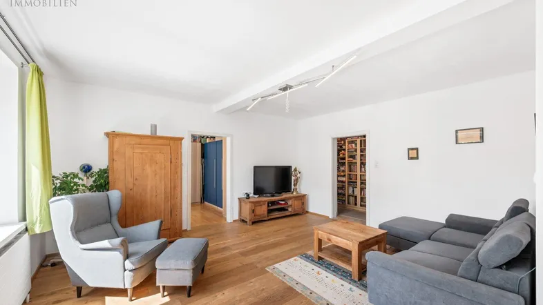 Helles Wohnzimmer mit Holzboden, gemütlicher Sitzecke und Blick auf einen Bücherraum.