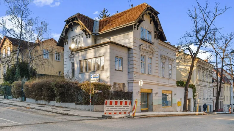 Historisches Gebäude an einer Straßenecke mit klassischer Architektur und Ziegeldach unter blauem Himmel.