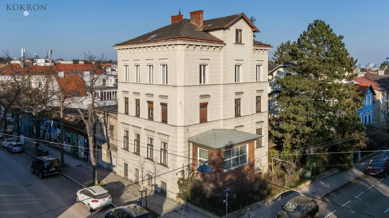 Luftaufnahme des historischen Gebäudes mit umliegender Straße und Bäumen bei sonnigem Wetter.
