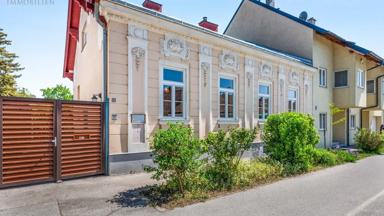 Historische Fassade eines Gebäudes mit dekorativen Elementen und einem Holztor zur Einfahrt.