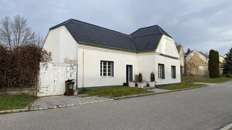 Einfamilienhaus von der Straße aus gesehen mit weißer Fassade und dunklem Dach, in ländlicher Umgebung.