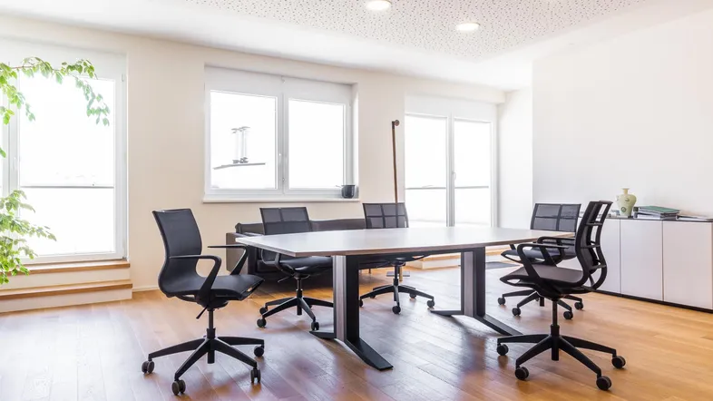 Heller Büroraum mit großem Konferenztisch, ergonomischen Stühlen und Holzboden, ideal für Besprechungen.