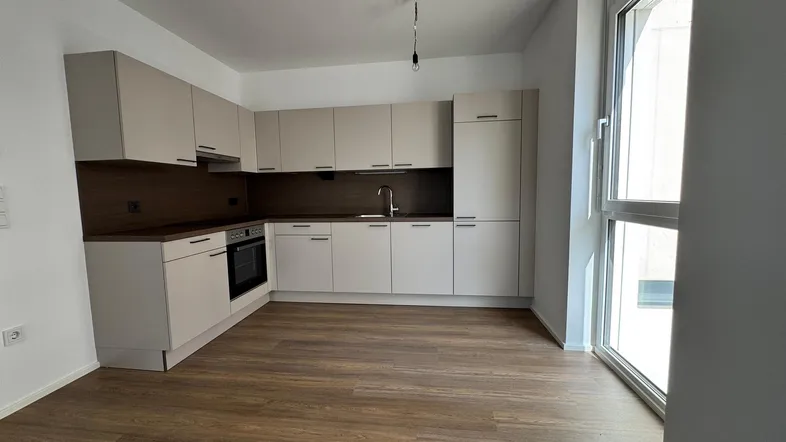 Moderne Einbauküche mit hellen Schränken, dunkler Arbeitsplatte und Laminatboden in einem hellen Raum.
